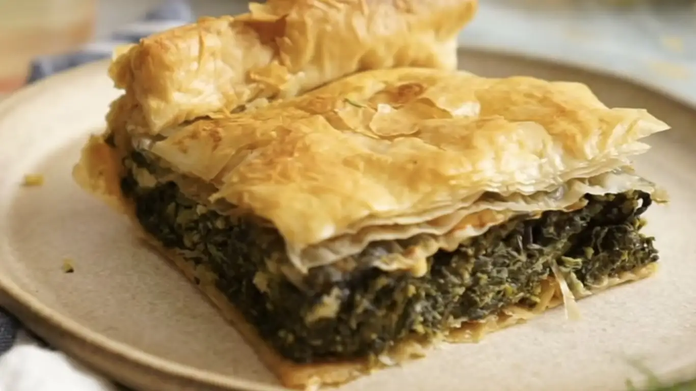 Homemade spinach stuffed pie with golden phyllo crust cut open to reveal layers of vibrant green spinach and feta cheese filling.